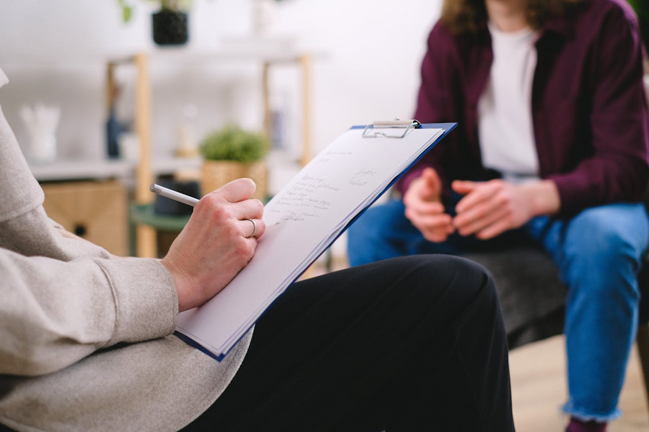 who-we-are Close-up of a therapist writing notes on a clipboard while conversing with a patient.